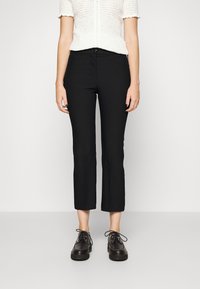 Pantalons noirs courts avec une coupe ajustée, en matériau lisse. Associés à des chaussures noires à lacets et un top en tricot blanc.