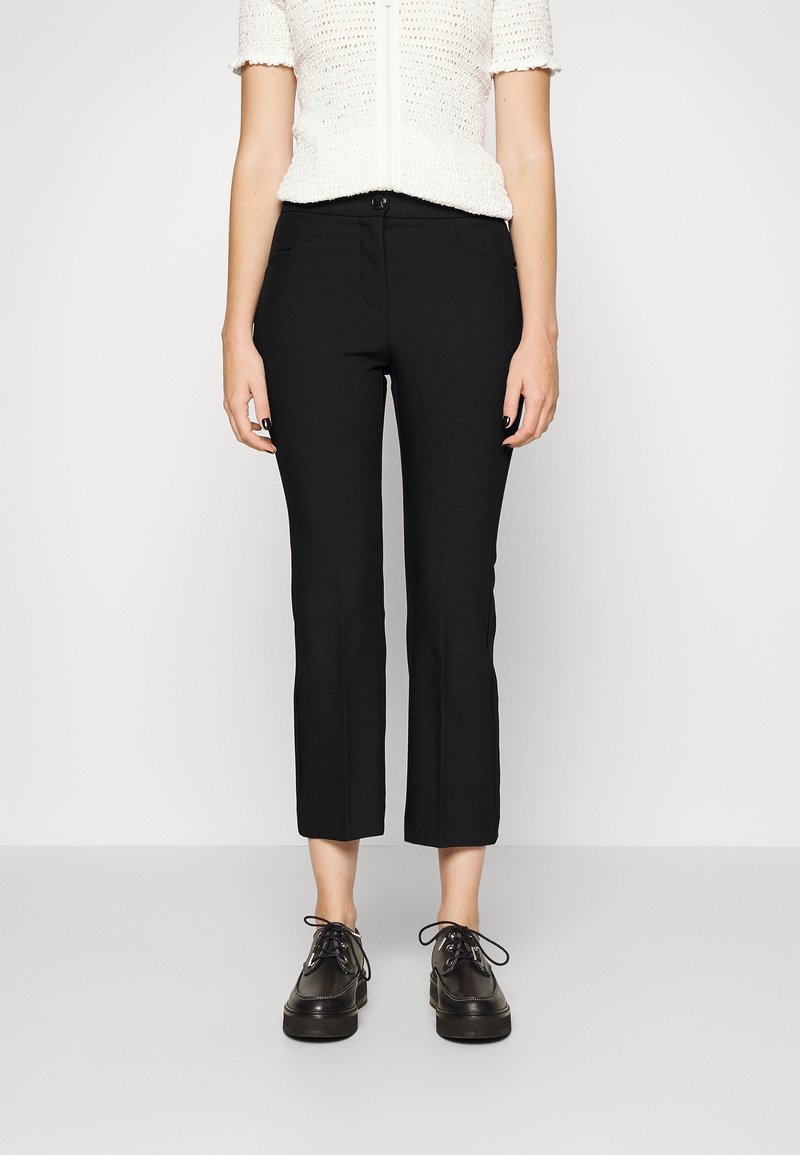 Pantalons noirs courts avec une coupe ajustée, en matériau lisse. Associés à des chaussures noires à lacets et un top en tricot blanc.