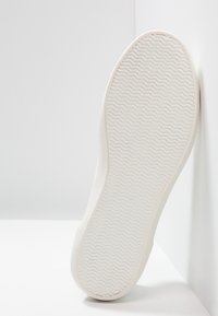 Valkoinen lenkkarin pohja, jossa on teksturoidun, aaltoilevan kuvion. Pyöreä kantapää ja muotoillut reunat, suunniteltu pitoa varten. Tasainen, siisti pinta.