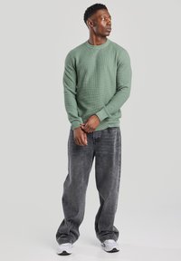 Green textured crew-neck sweatshirt paired with faded black loose-fit jeans and white sneakers, featuring ribbed cuffs and hem details.