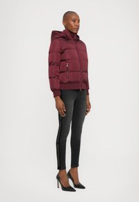 Burgunderrød puffjakke med hette, quiltet design og glidelåslomme. Kombinert med svarte skinny jeans med sidemerking og svarte heler.