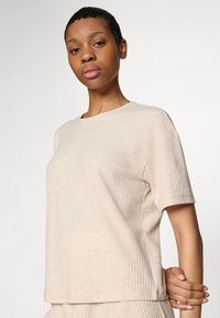 Beige struktureret kortærmet skjorte med rund hals, der har et diskret ribbet mønster. Stoffet ser blødt og let ud.
