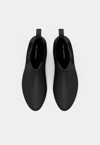 Sapatos pretos tipo slip-on com um acabamento suave e mate, ponta arredondada e design recortado no tornozelo. Inclui uma alça para facilitar o calçar.