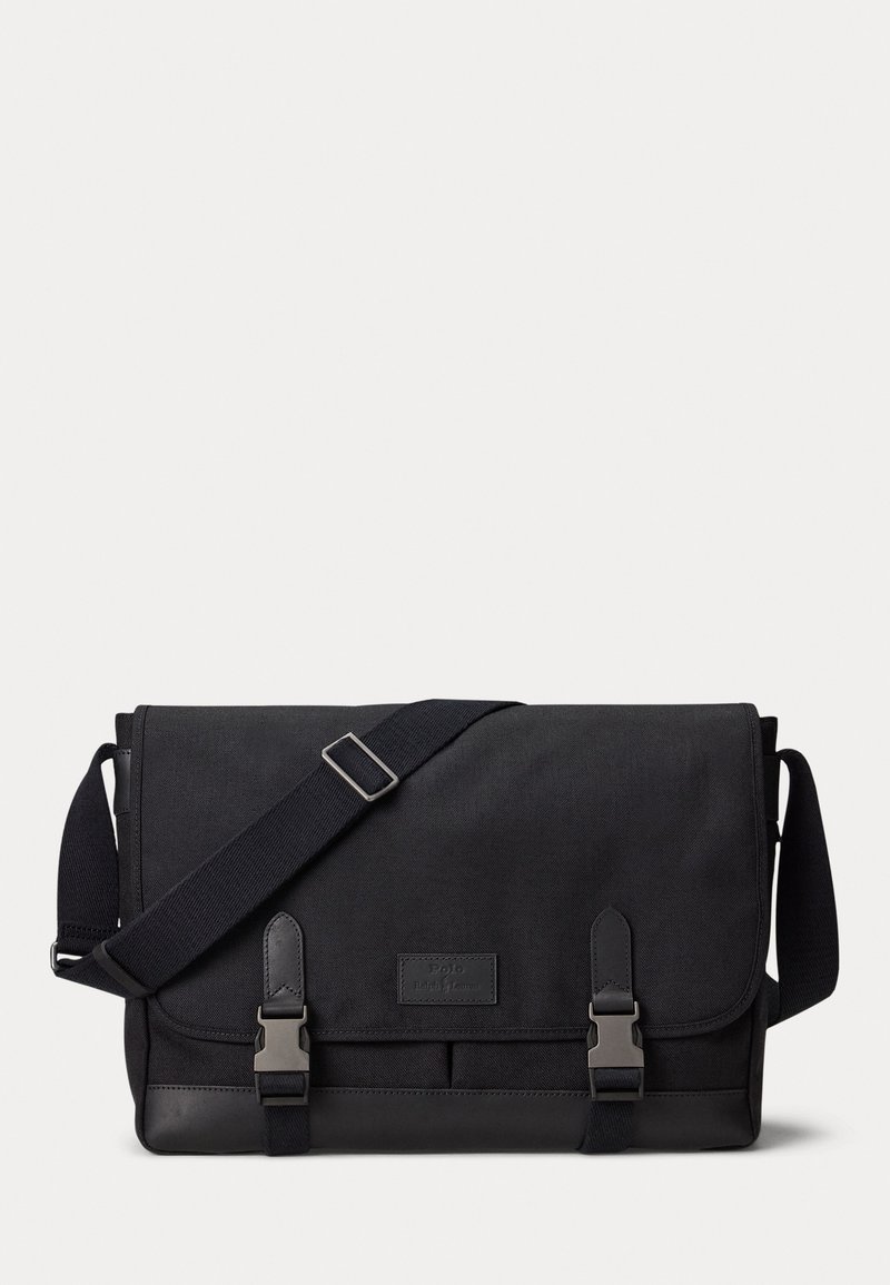 Borsa a tracolla nera realizzata in tessuto resistente, con chiusura a pattina, cinturino regolabile e accessori in metallo argentato con due fibbie.