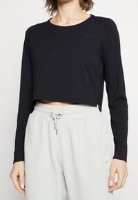 Black long-sleeve cropped top with a round neckline. Soft material and subtle logo detail; paired with light grey sweatpants featuring pockets.