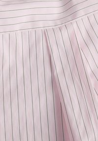 Hele-roosa kangas, millel on õhukesed vertikaalsed mustad triibud ja õmmeldud laskmed, mis loovad tekstuuri mustri.