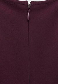 Bordeaux-vaate, jossa on hienovarainen tekstuuri, näkyvällä vetoketjulla takana. Yksinkertainen, slim fit -muotoilu ilman lisäkoristeita tai kuvioita.