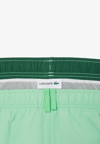 Shorts de bain verts avec une taille élastique, doublure en maille intégrée et une étiquette de logo Lacoste. Surface texturée avec un éclat subtil.