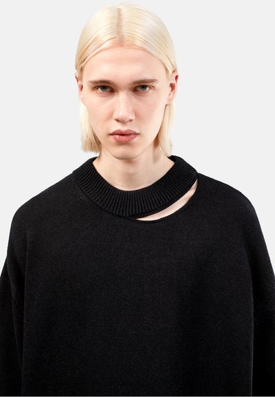 Svart stickad tröja med en bred ribbad krage och en distinkt utskärning fram. Mjuk textur och avslappnad passform.