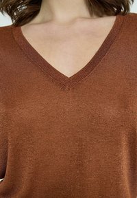 T-shirt s kratkimi rokavi v obliki črke V iz sijočega bronastega materiala. Teksturna površina z rahlim sijajem poudarja moden in sproščen kroj.