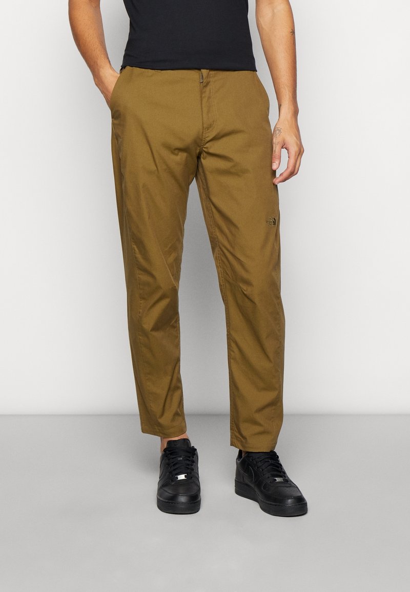 Kalhoty z bavlněné směsi v khaki hnědé barvě s předním zapínáním na zip, rovným střihem a jemným logem na boku. Kombinované s černými teniskami.
