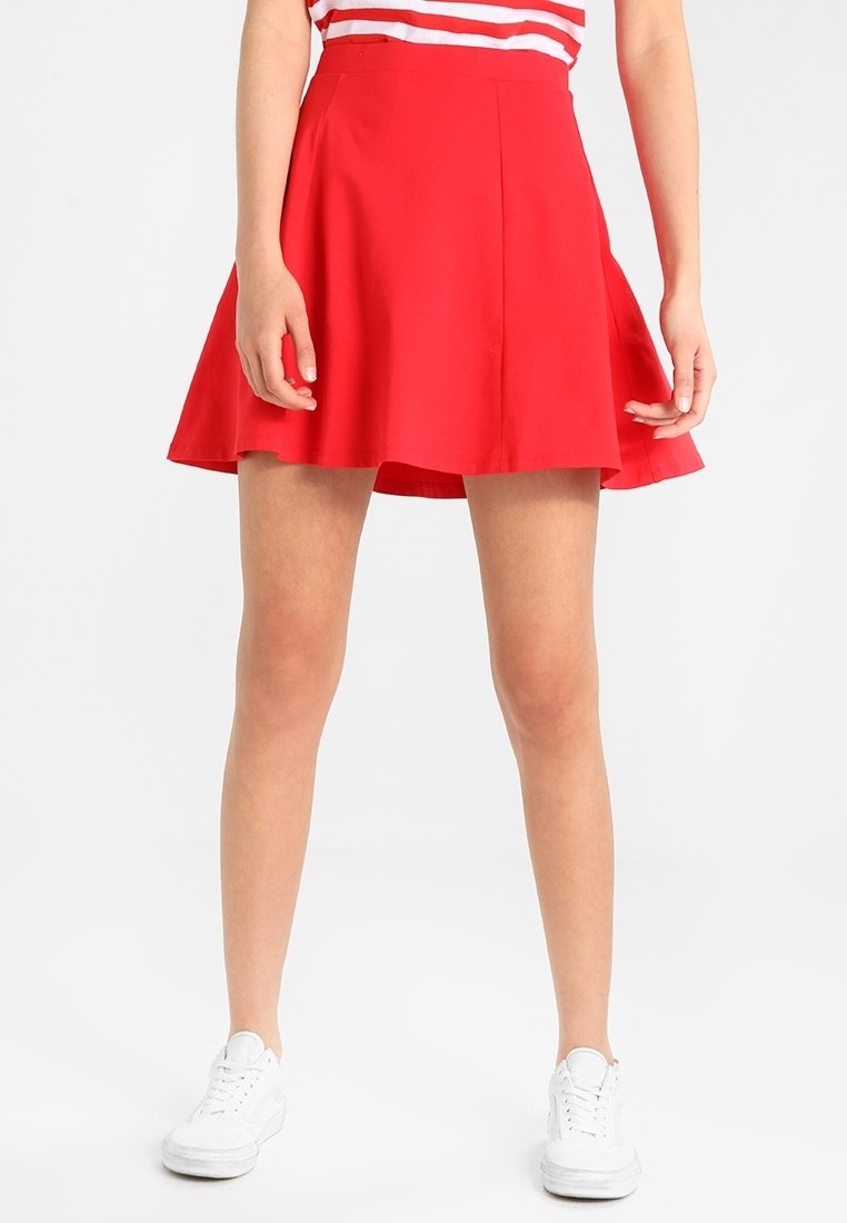 Roter, ausgestellter Rock aus leichtem Stoff, mit einem taillierten Bund und fließendem Design. Kombiniert mit einem gestreiften Oberteil und weißen Sneakers.