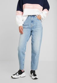 Vaqueros de tiro alto de color azul claro con un corte recto, combinados con una sudadera de rayas en azul marino, blanco y rosa que presenta la marca "TOMMY JEANS".