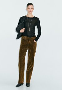 Pantalons en velours côtelé marron associés à un haut noir à manches longues et un sac à épaule, avec un simple collier en pendentif argenté. Texture lisse.