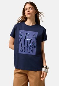 T-shirt en coton bleu marine à manches courtes, avec un motif en sequins bleu clair et noir sur un carré violet portant l'inscription "MER AIR & SOLEIL".