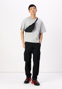 Grå oversized t-shirt, sorte cargo bukser med sidelommer og sorte/røde sneakers. Sort crossbody taske med justerbar rem.