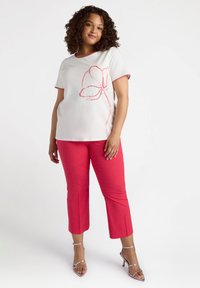 Top blanco con bordado floral rojo y mangas cortas, combinado con pantalones cortos rosa con pequeños embellishments, usados con zapatos de tacón plateados.