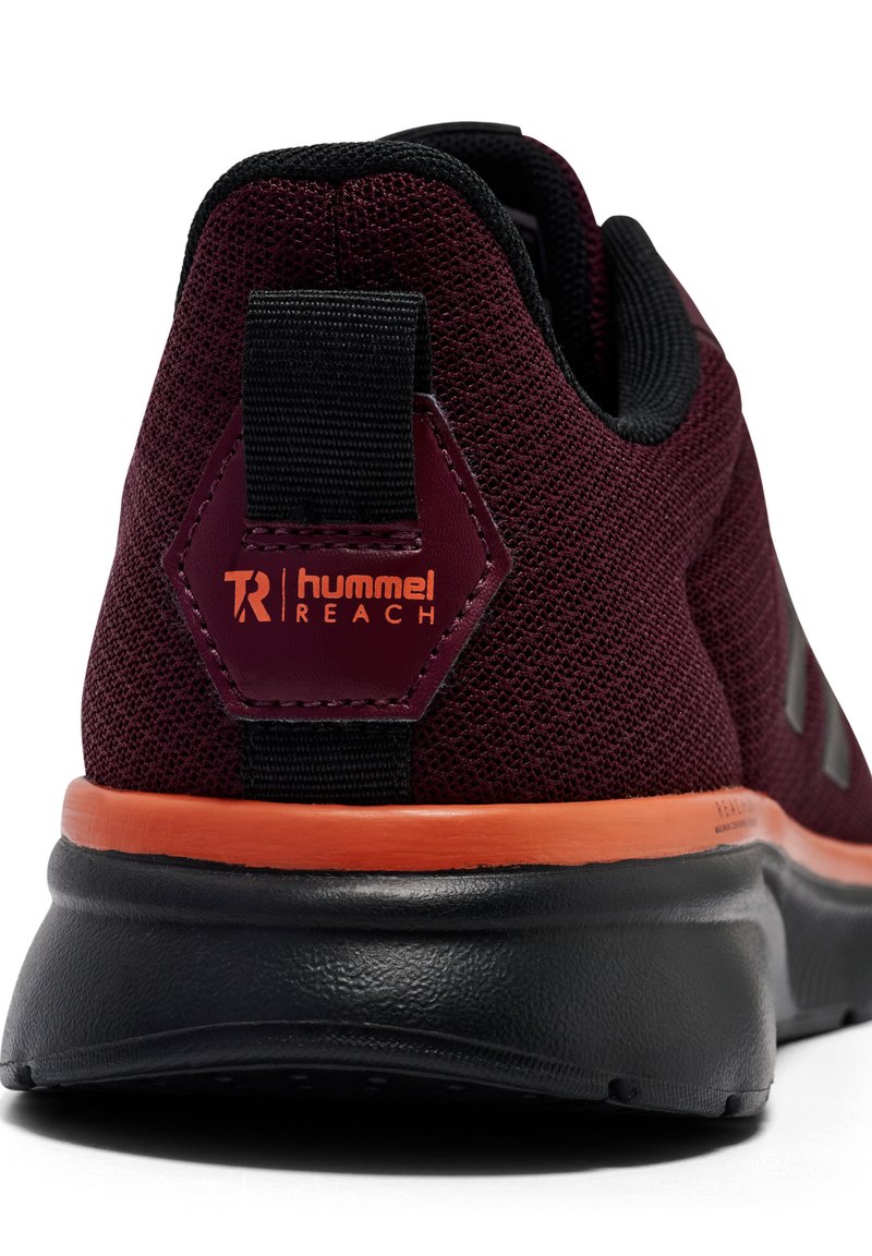 Zapatilla deportiva color burdeos con parte superior de malla, un tirador negro en el talón y un acento naranja a lo largo de la suela. Presenta un detalle de marca hexagonal.