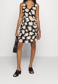 Černé květinové šaty bez rukávů, zdobené broskvovými růžemi a zelenými listy. Doplněné černou kabelkou a černými sandály na podpatku.