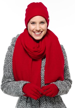 Punane kudumine beanie, sall ja kindad on ühendatud halli, mustrilise mantliga. Sall ja kindad on pehmed, luues ühtse talvise ilme.