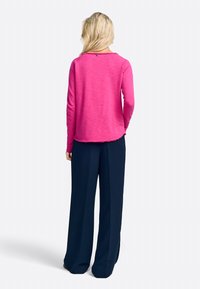Langärmliges pinkes Oberteil mit einem runden Halsausschnitt, kombiniert mit navyblauen weitem Hosen. Das Oberteil hat einen strukturierten Stoff und einen rohen Saum.