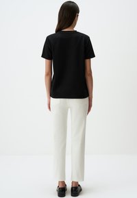 Zwarte korte mouwen t-shirt, eenvoudig ontwerp, met een ronde halslijn, gecombineerd met witte rechte broek, uitgerust met zakken en een gladde textuur.