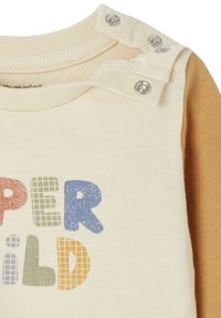 Langärmliges Shirt mit einem cremigen Körper und orangefarbenen Ärmeln, rundem Ausschnitt und Druckknöpfen. Der Text in bunten, fetten Buchstaben lautet "SUPER KIND."