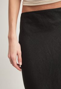 Pogled od blizu na lijevu ruku osobe koja se odmara pored crne suknje i bež kratkog topa, prikazujući ton kože i teksturu tkanine.