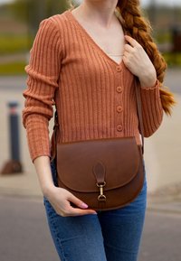 Cardigan a coste color ruggine con dettagli a bottoni, abbinato a una borsa a tracolla in pelle marrone con chiusura e pattina arrotondata.