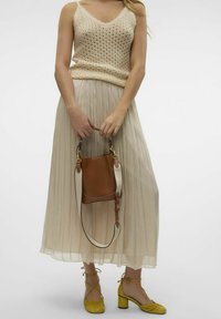 Beige stickad linne med tunna axelremmar, flödande plisserad krämfärgad kjol, gula klackskor och en brun bucket bag med en vit rem.