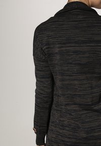 Stickad tröja i mörkblått och grått med ett strukturerat randmönster, med en mock-krage och knappprydda manschetter.