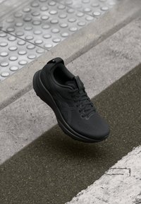 Baskets de course noires avec une tige en mesh respirant, surface texturée et semelle rembourrée. Présente des lacets et une languette au talon pour un enfilage facile.