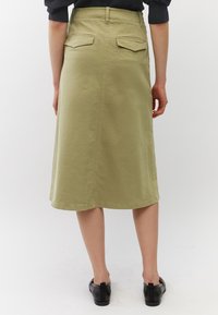 Khaki midi rok met een rechte snit, twee achterzakken en zichtbare stiksels. Draagt met zwarte platte schoenen. Glad, katoenmateriaal.