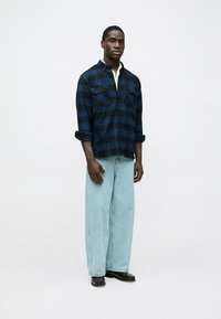 Marinų ir juodų languotų marškinėlių su sagomis, turinčių dvi krūtinės kišenes. Derinami su šviesiai mėlynais plačiomis kojomis džinsais ir juodais batais.