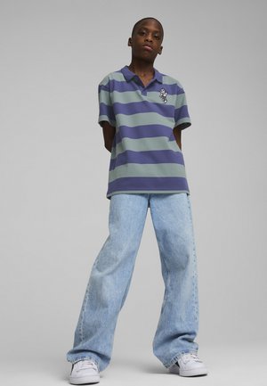 Polo a righe verde e viola con logo sul petto, abbinato a jeans in denim azzurro chiaro larghi e sneakers bianche.