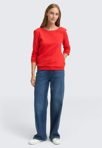 Rode sweatshirt met een ronde halslijn, lange mouwen en ribbelmanchetten, gecombineerd met brede blauwe jeans en witte sneakers.