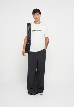 Wit T-shirt met zwarte branding, donkere wijde broek en een zwarte crossbodytas. Accessoires omvatten een zilveren ketting.