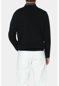 Schwarzer Strickpullover mit blauer Kragen, langen Ärmeln und geripptem Saum, kombiniert mit weißen Hosen. Texturierter Stoff mit lockerer Passform.