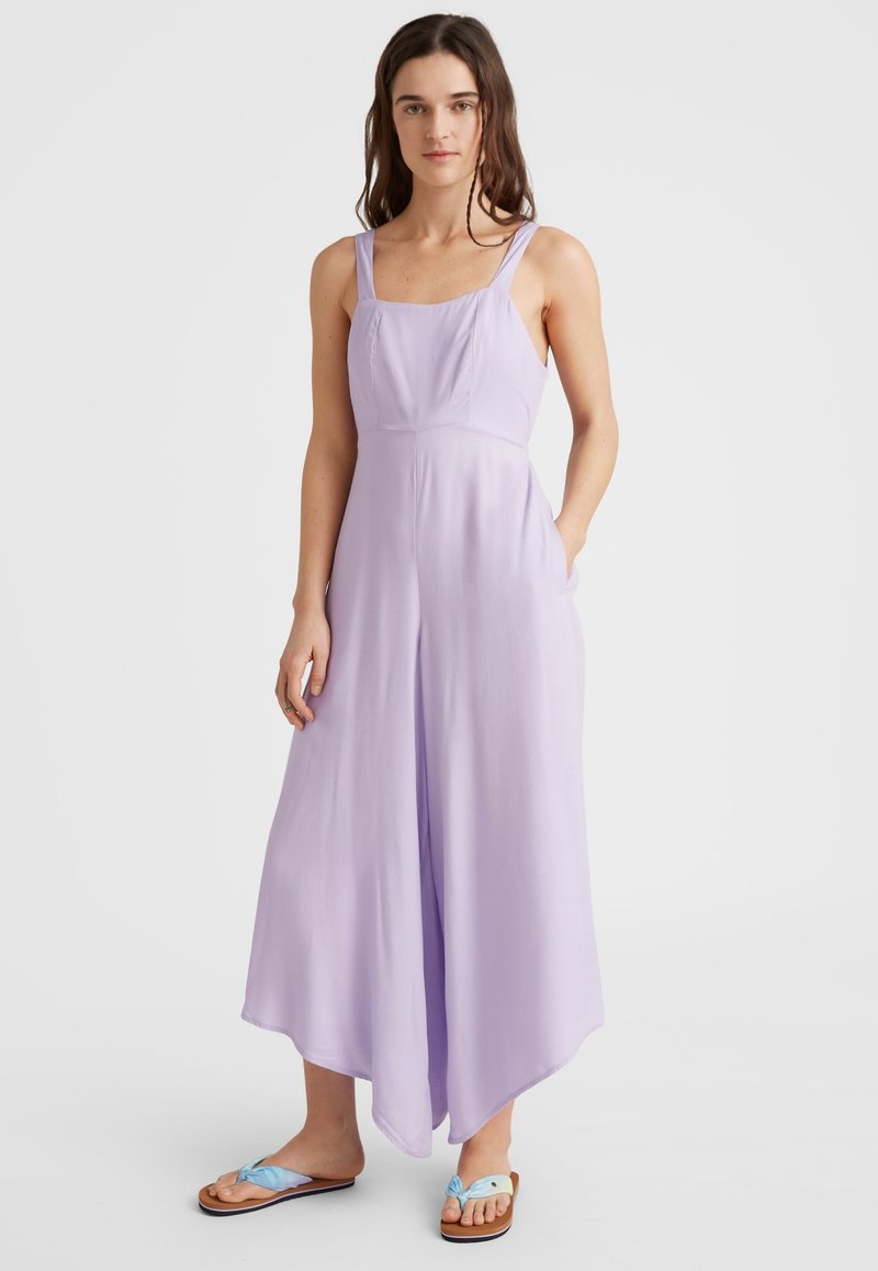Lila ärmelloser Jumpsuit mit weitem Bein, subtilen Nähten und Taschen; kombiniert mit braunen Flip-Flops mit hellblauen Akzenten.
