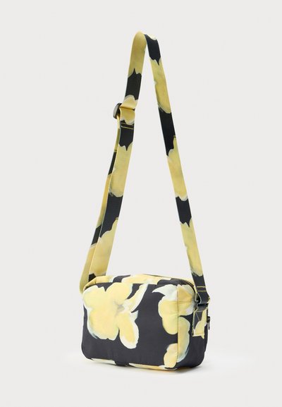 Floral crossbody bag with a black background and yellow flower pattern. Features a long adjustable strap and a zip closure. Textured fabric.