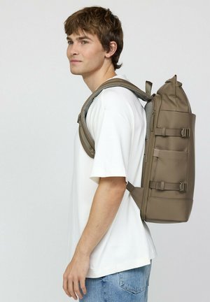 Der khakifarbene Rucksack verfügt über eine zylindrische Oberseite, verstellbare Träger und mehrere Seitentaschen. Er ist aus robustem, wasserabweisendem Material gefertigt.