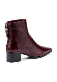 Botas de tobillo de cuero burdeos con punta afilada, tacón bajo en bloque y cremallera lateral con un acento de hardware circular. Textura suave.
