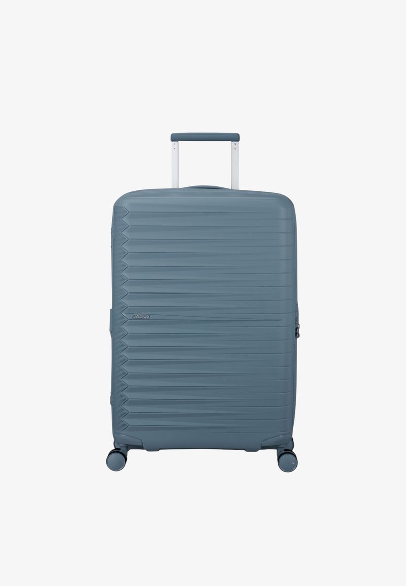 Maleta rígida de color azul claro con textura acanalada horizontal, asa retráctil y cuatro ruedas giratorias para facilitar la maniobrabilidad.