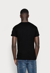 Czarna bawełniana koszulka z krótkim rękawem, okrągłym dekoltem; noszona z niebieskimi dżinsami z tylnymi kieszeniami i delikatnym efektem blaknięcia.