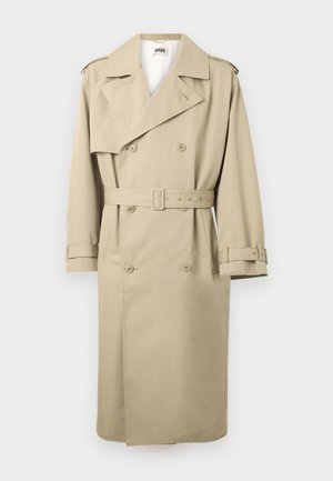 Beige dobbeltbrystet trenchcoat med brede revers, taljet med bælte, skulderepåletter og justerbare håndledsremme, hængende fladt mod hvid baggrund.