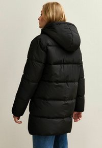 Cappotto imbottito nero con cappuccio, caratterizzato da sezioni orizzontali trapuntate e maniche lunghe. Il tessuto ha una consistenza liscia e un design elegante.