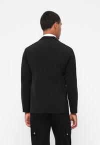 Sort letvægtsjakke med lange ærmer, en spids krave og minimal detaljer. Bagsiden har et glat, strømlinet design.