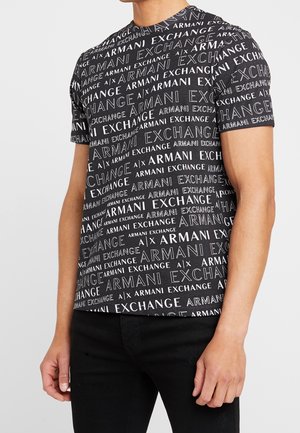 Camicia nera a maniche corte con testo bianco "Armani Exchange" in caratteri vari indossata da una persona con pantaloni neri, braccia rilassate lungo i fianchi.