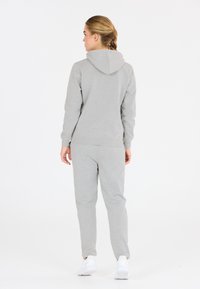 Jasnoszara bluza z kapturem i dresy wykonane z miękkiego materiału. Posiadają regulowany kaptur i ściągacze na rękawach. Noszone z białymi trampkami.