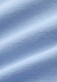 Ljusblått tyg med en slät textur och ett fint ribbat mönster, som visar upp mjukt, stretchigt material med en subtil lyster.